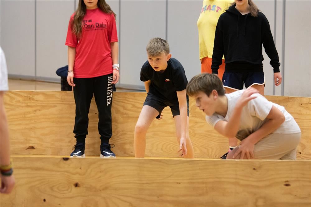  Several students play a ball game inside of a wooden frame.